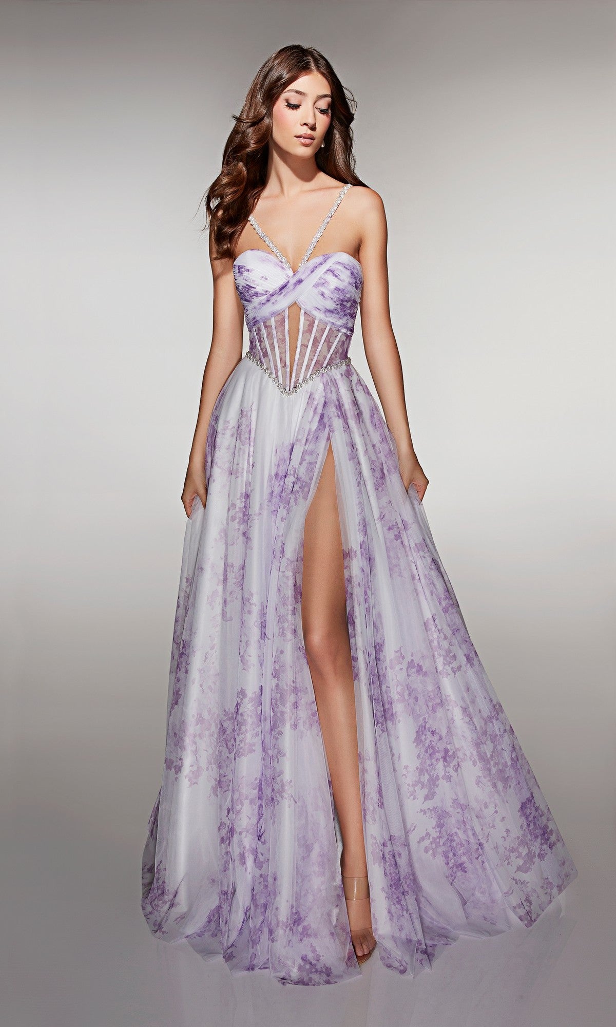 A woman models the Alyce 61994 long prom dress—lavender floral, floor-length, with a corset bodice, thin straps, and a high leg slit—against a plain background.